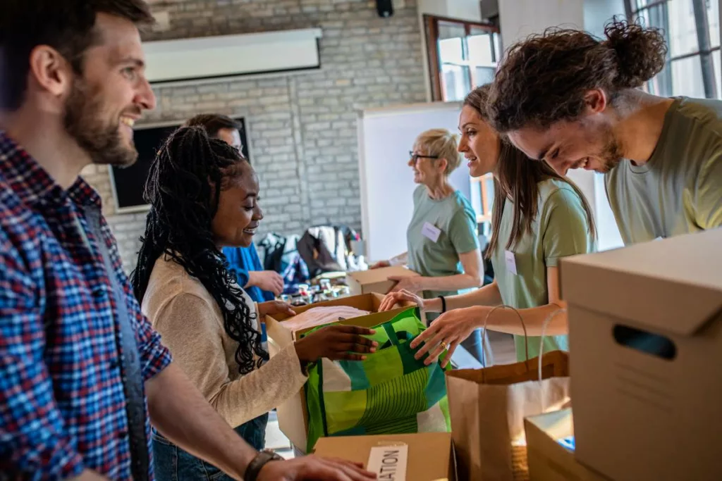 Freiwillige Mitarbeiter arbeiten gemeinsam an einem Corporate Volunteering Projekt indem sie Spendenpakete für gemeinnützige Zwecke vorbereiten