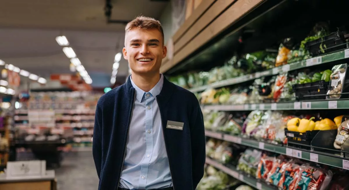 Ein lächelnder junger Mann steht in einem Supermarktgang. Geringfügigkeitsgrenze: Die Grenze der Minijobber.
