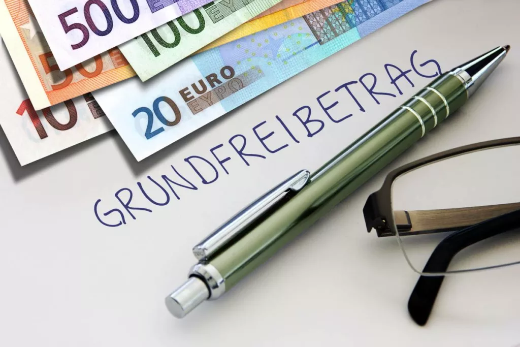 Grundfreibetrag: Euro-Geldscheine, Stift und Brille als Symbole für Steuerfreibetrag.